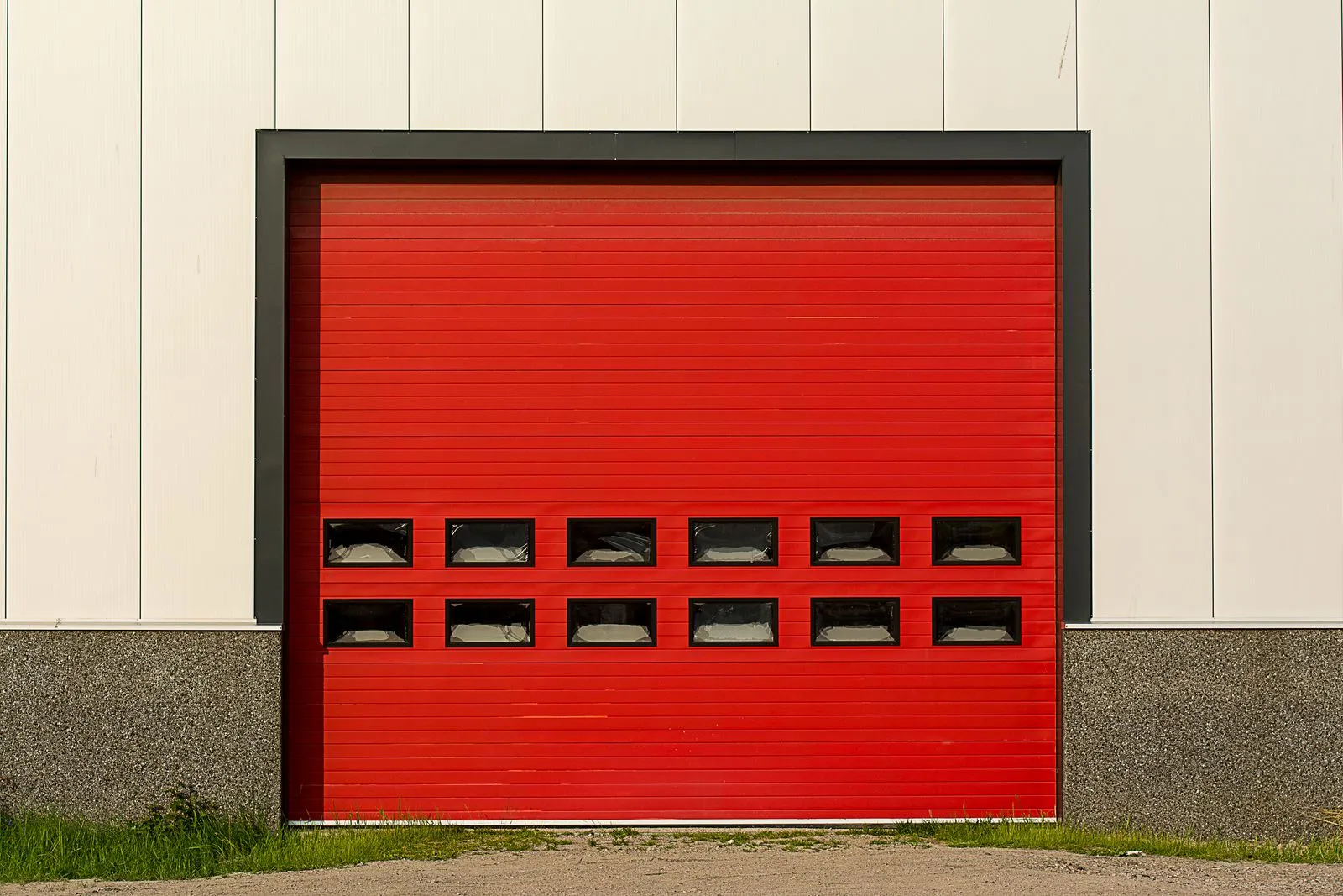Bright red roller shutter garage door on industrial building exterior.